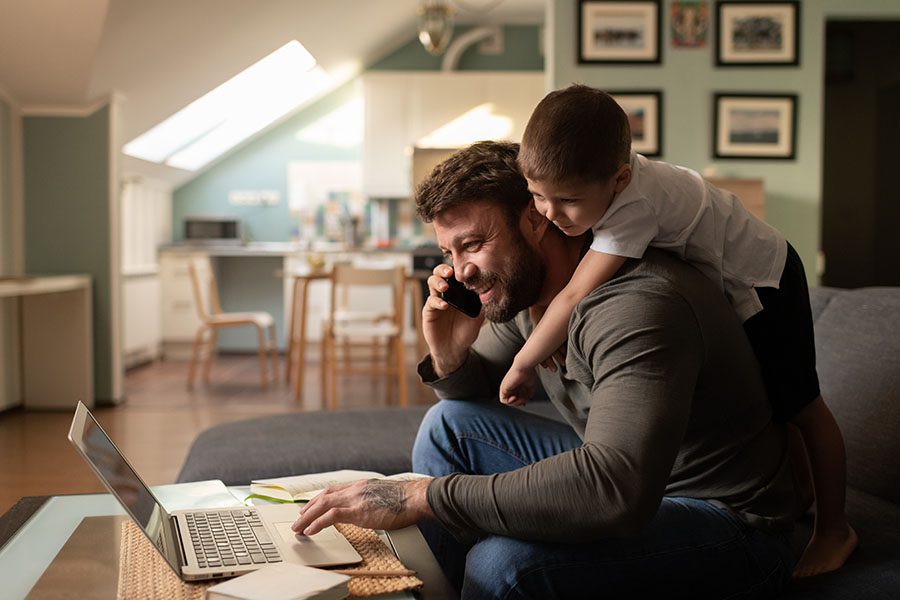 Contact - Father Happily Using a Laptop and Cell Phone While Son Hangs on His Back